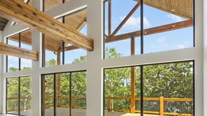 A spacious interior with large windows, wooden beams, and a view of an outdoor deck. - Lakeview Getaway | 6BR Near Table Rock (Cape Fair)