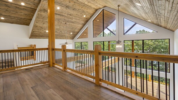 A spacious interior with wooden flooring, a high ceiling with exposed beams, and large windows offering views of the outdoors. - Lakeview Getaway | 6BR Near Table Rock (Cape Fair)