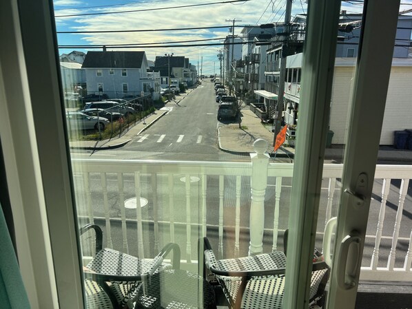 Une vue depuis une fenêtre donnant sur une rue où sont garées des voitures, avec des bâtiments et un ciel dégagé.