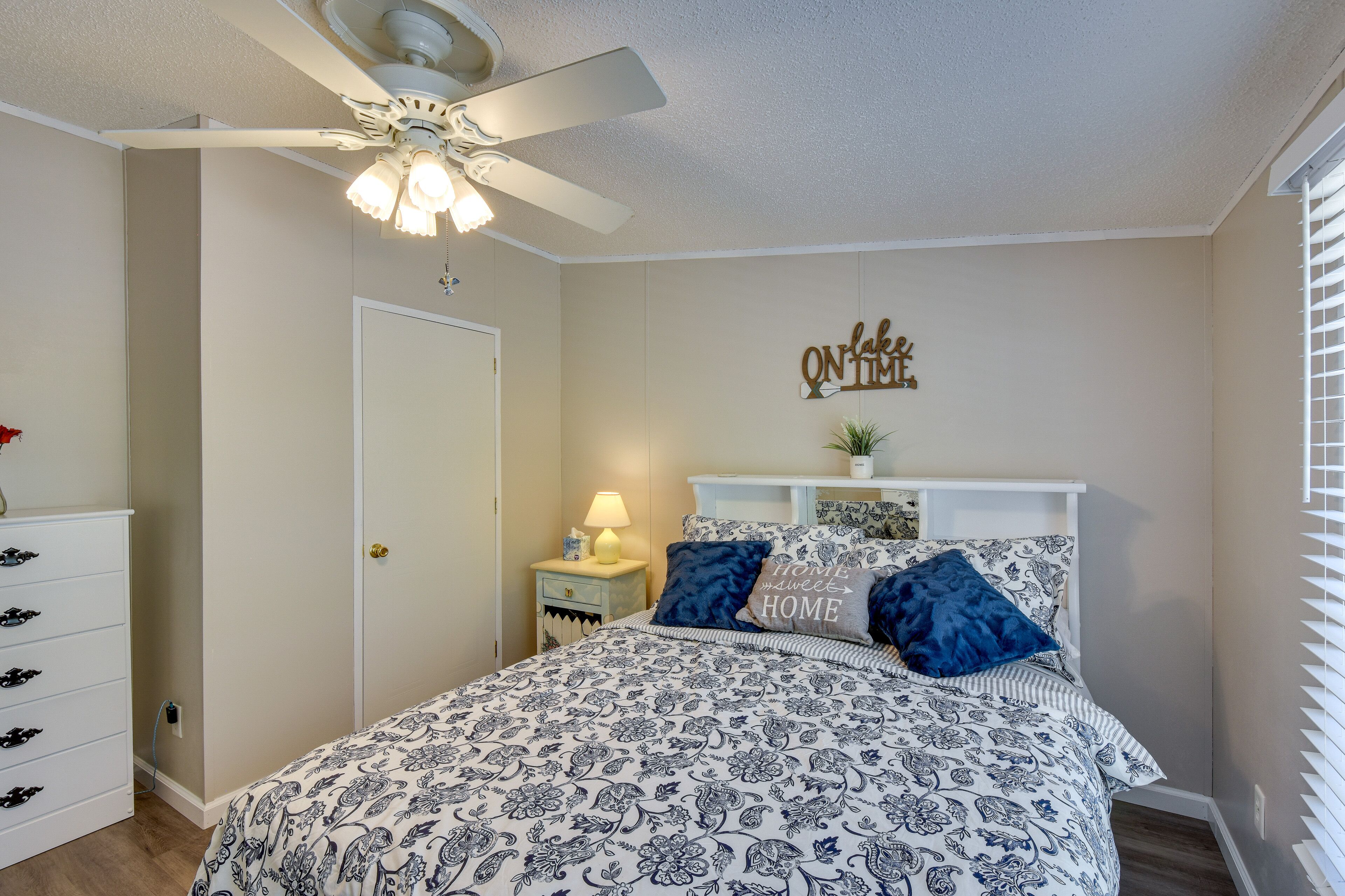 A bedroom with a bed, a nightstand, a dresser, a ceiling fan, and a wall decoration.