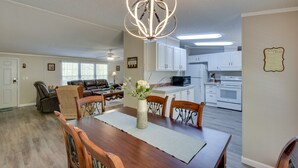 A dining area with a wooden table, chairs, and a vase of flowers. There is a kitchen in the background with white cabinets and appliances. - Walk to Lake Chatuge! Hayesville Cabin w/ Fire Pit (Hayesville)