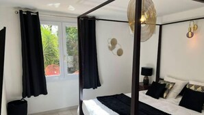 A four-poster bed with black bedding, a round wall light, and a view of greenery outside. - Villa de Luxe, Hyper Centre, Port de Portovecchio (Porto-Vecchio)