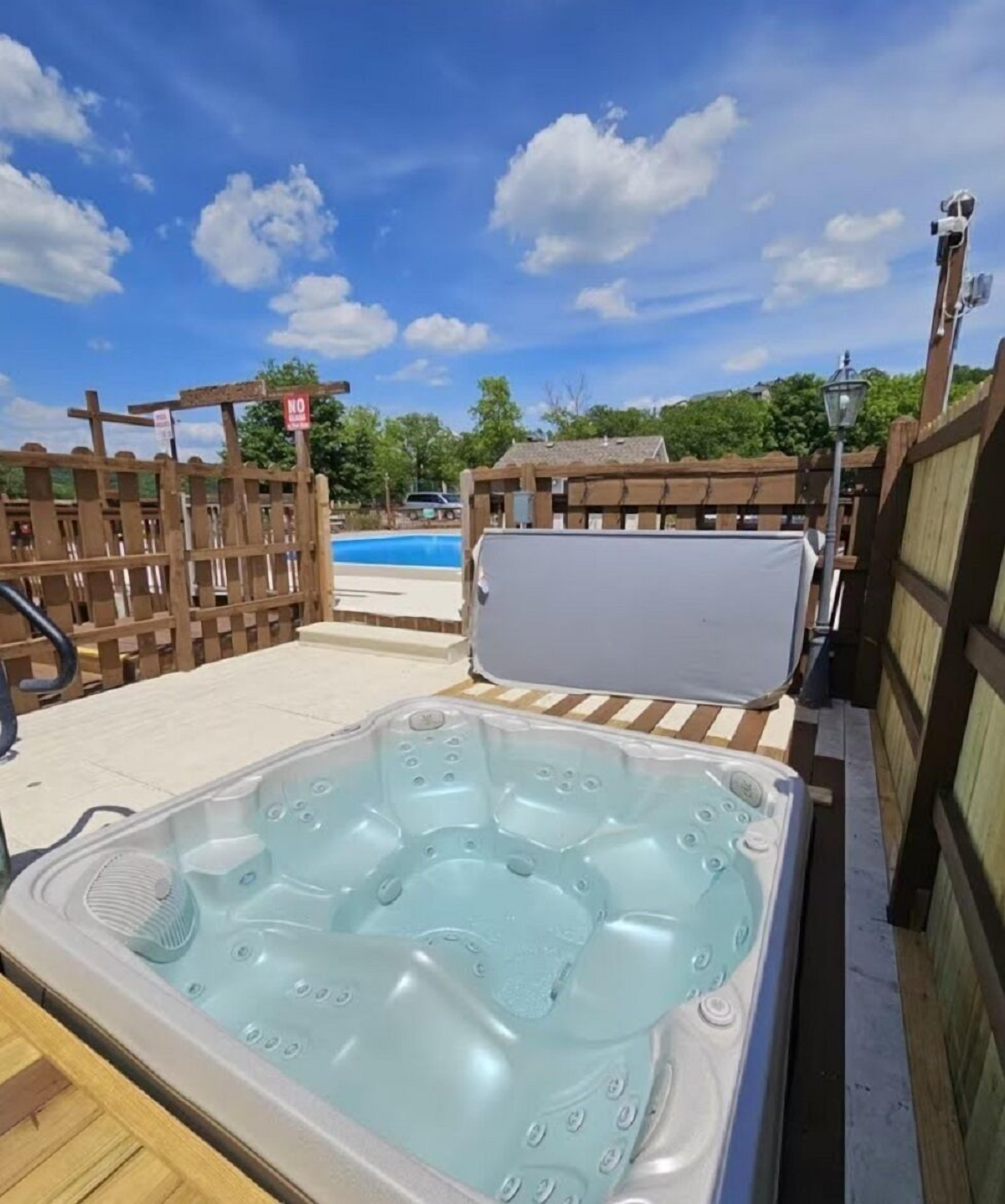 Ein Whirlpool mit einer Holzdielen-Terrasse und einem Pool im Hintergrund.