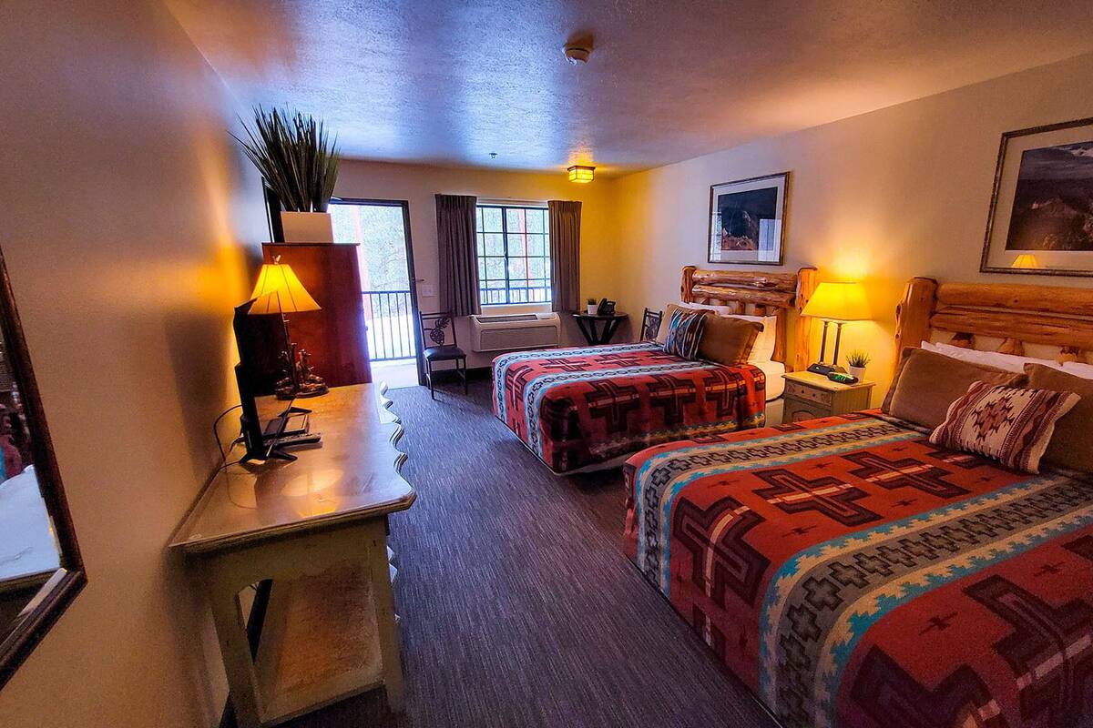 A hotel room with two beds, a desk, a chair, a lamp, a window, and a painting on the wall.