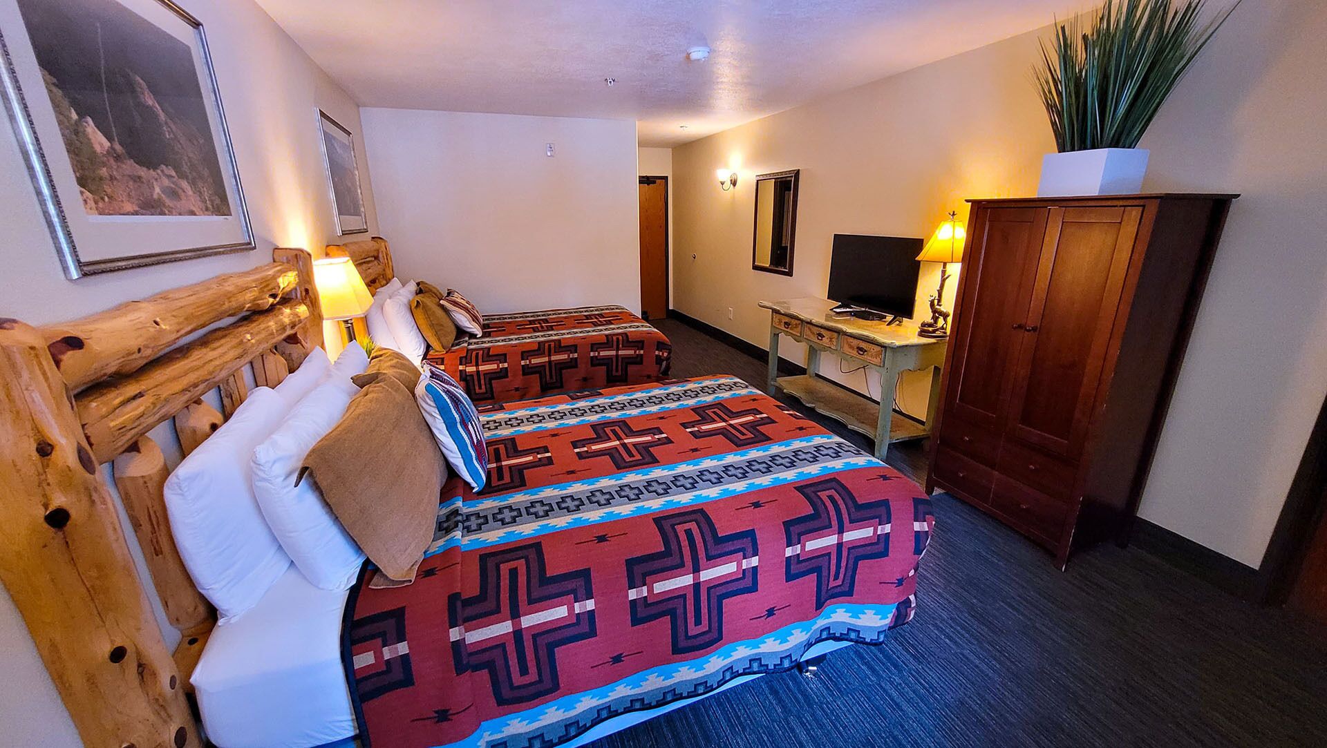Une chambre d’hôtel avec une tête de lit en bois, un lit avec une literie à motifs, un bureau avec une télévision et une armoire.