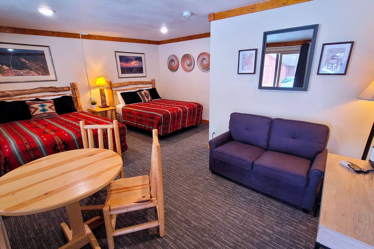 A hotel room with two beds, a sofa, a table, and a chair.