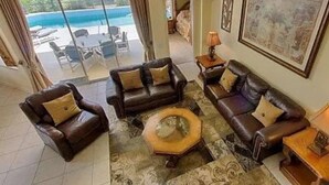 Ein geräumiges Wohnzimmer mit Ledersofas, einem Couchtisch und einem großen Fenster mit Blick auf einen Pool.