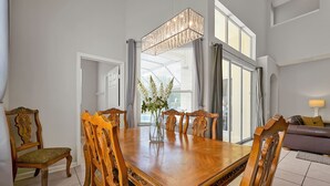 Ein Essbereich mit Holztisch und Stühlen, einer Blumenvase und einem großen Fenster mit Vorhängen.