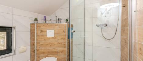 Une salle de bain avec un meuble-lavabo en bois, des toilettes, une douche en verre et un luminaire fixé au mur.