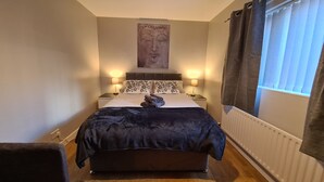 A bedroom with a bed, two bedside lamps, a wall-mounted artwork, a radiator, and a window with curtains. - Rutland Street Townhouse Belfast (Belfast)