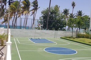 An outdoor basketball court with a net, surrounded by a fence and palm trees. - Beachfront Lux Gem in  of Isla Verde  Walk 2 Eat (Carolina)