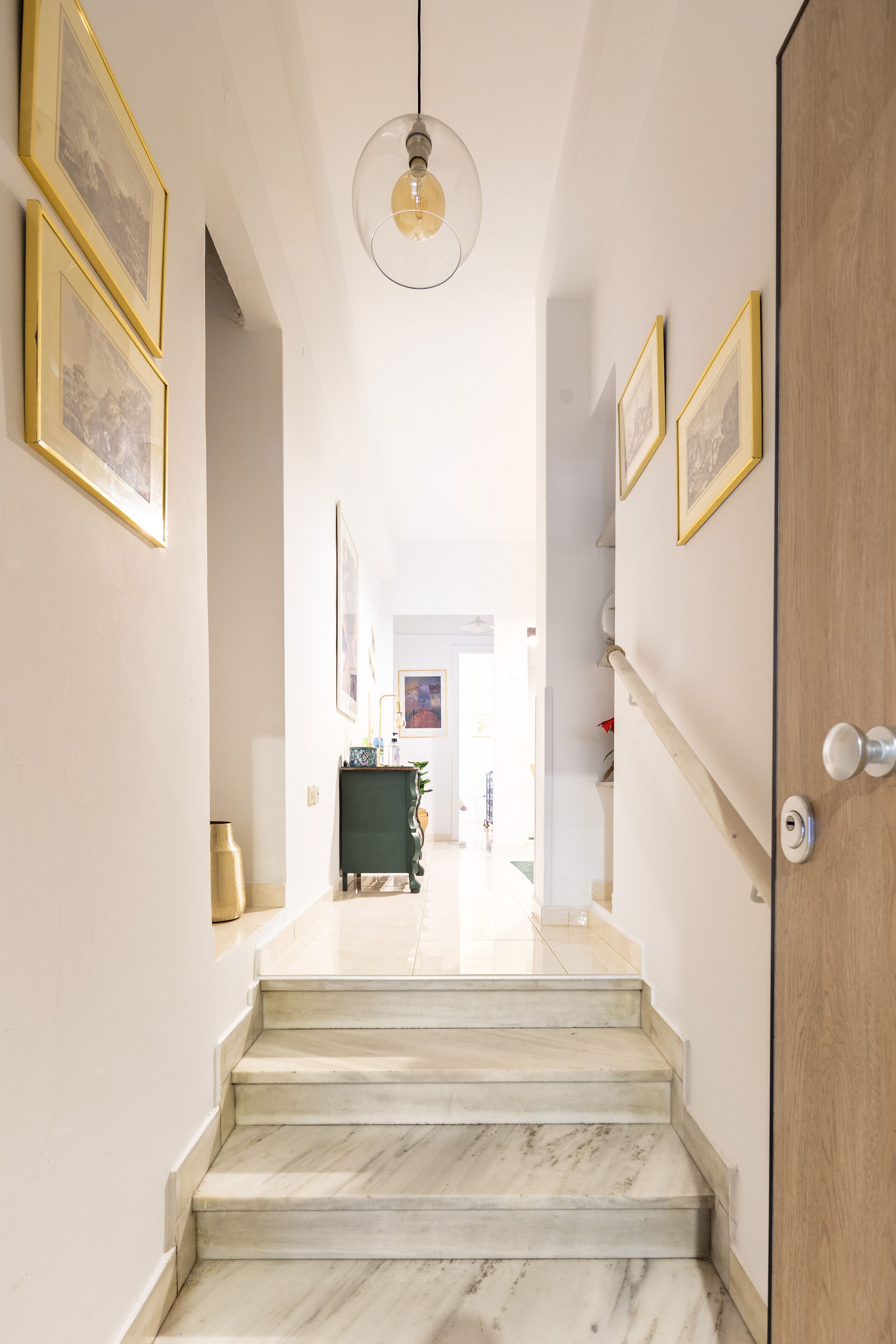 A staircase leading to a room with a wooden door, framed pictures on the walls, and a hanging light fixture.