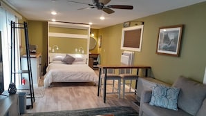 A room with a bed, a sofa, a table, and a ceiling fan.