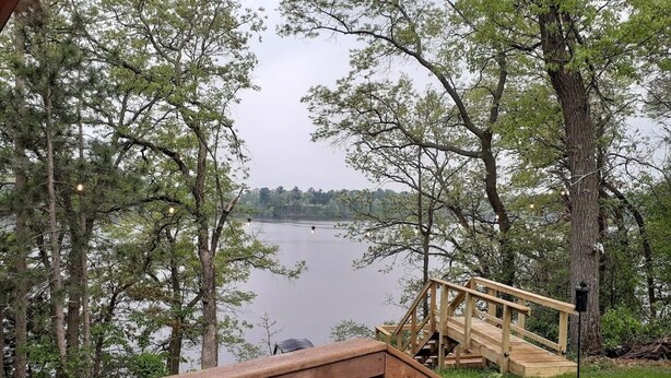 A wooden deck with a staircase leading to a dock over a lake, surrounded by trees.