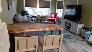 A living room with a wooden dining table, two chairs, a red armchair, a TV, and a fireplace.