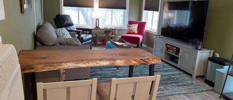 A living room with a wooden dining table, two chairs, a red armchair, a TV, and a fireplace.