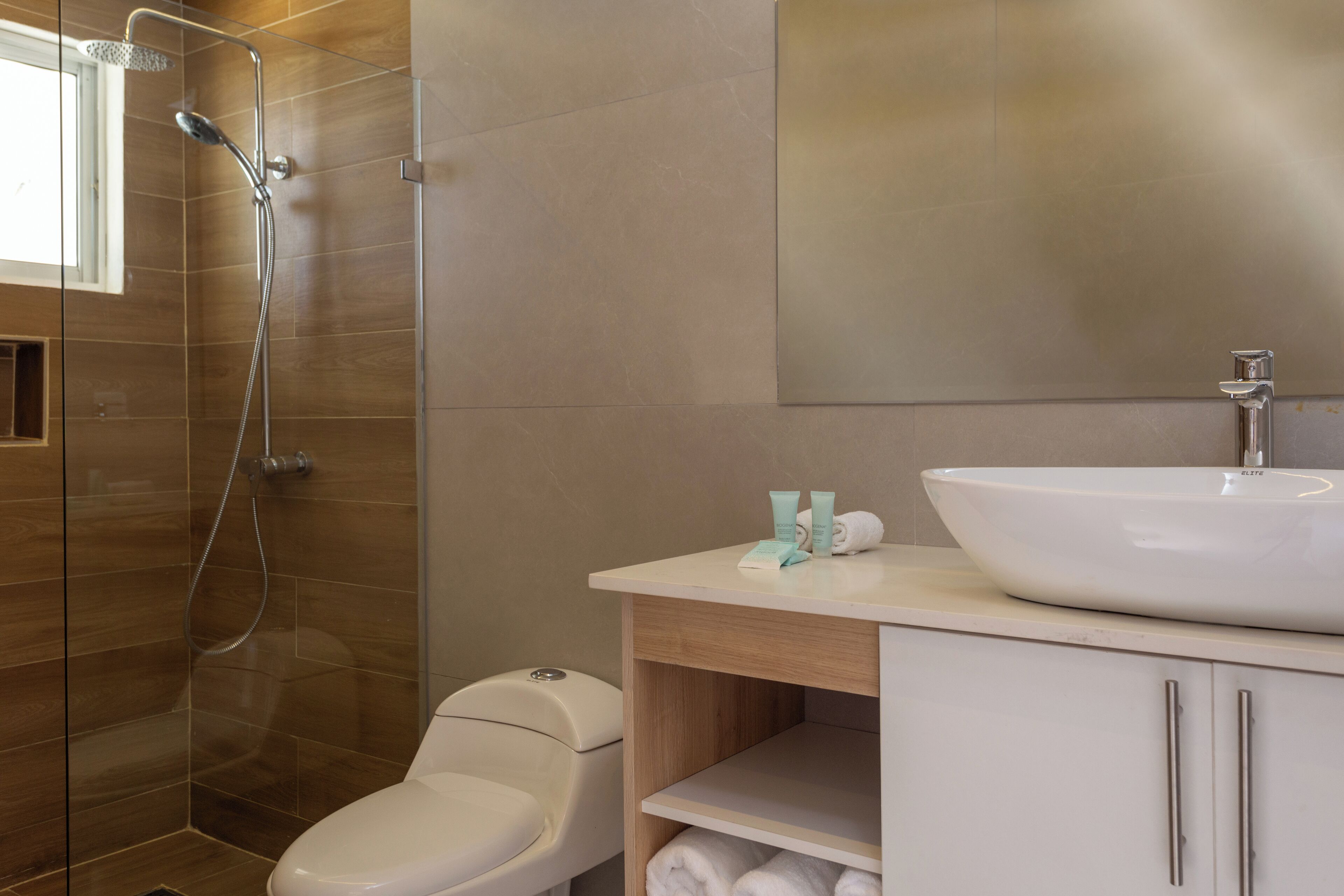 Een moderne badkamer met een douche met glazen wand, toilet, wastafel met spiegel en een plank met handdoeken.