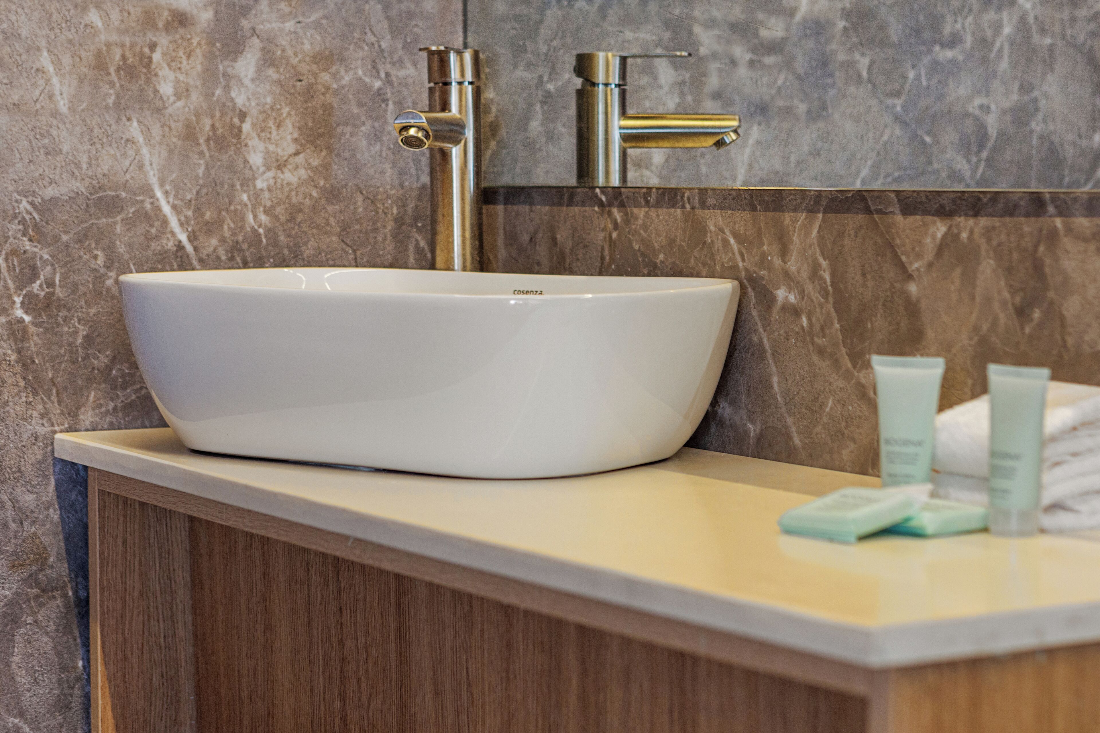 A bathroom with a white vessel sink, wooden cabinetry, and a marble backsplash.