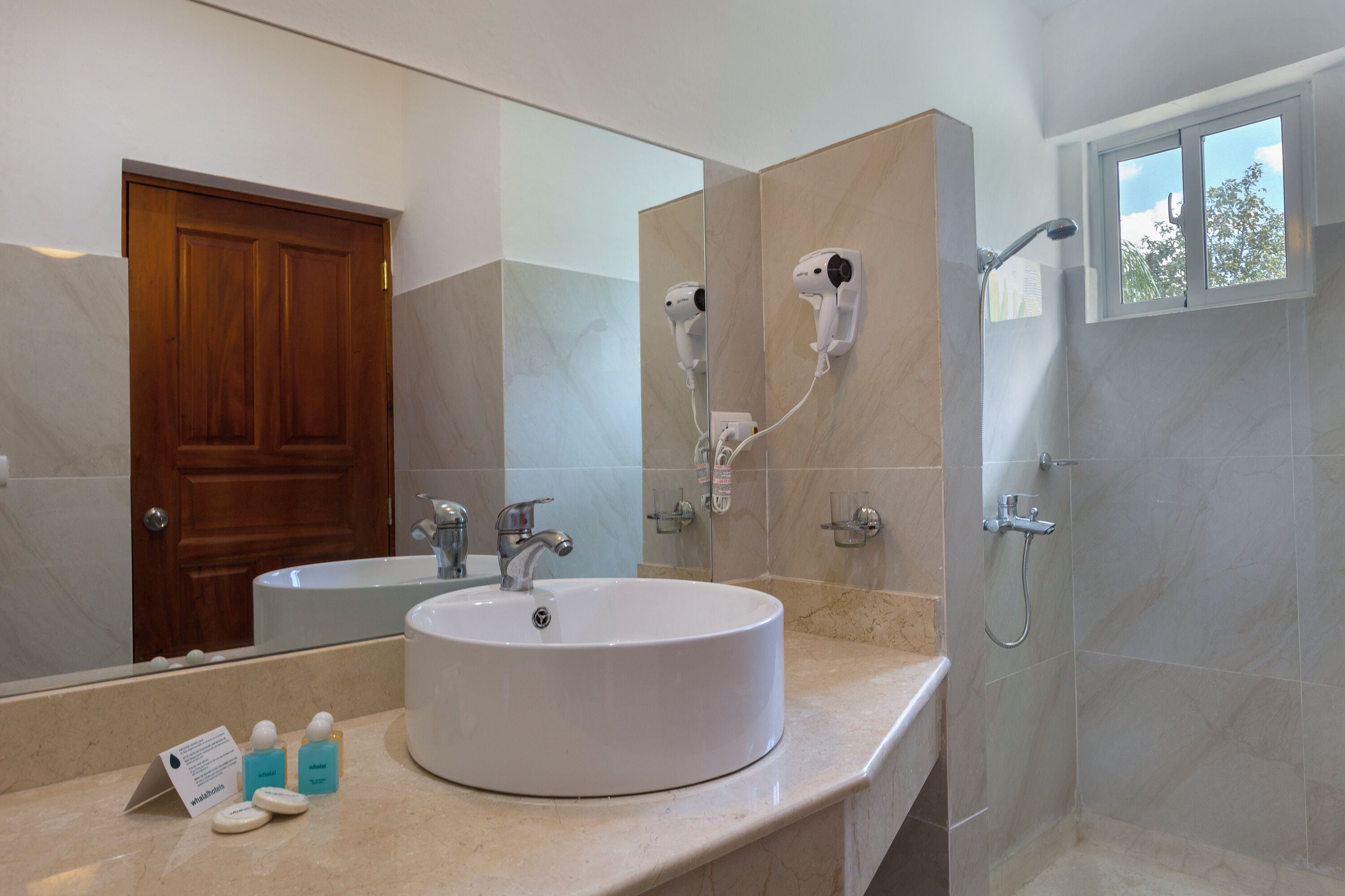 Une salle de bain avec un lavabo rond, un miroir, un sèche-cheveux et une douche.