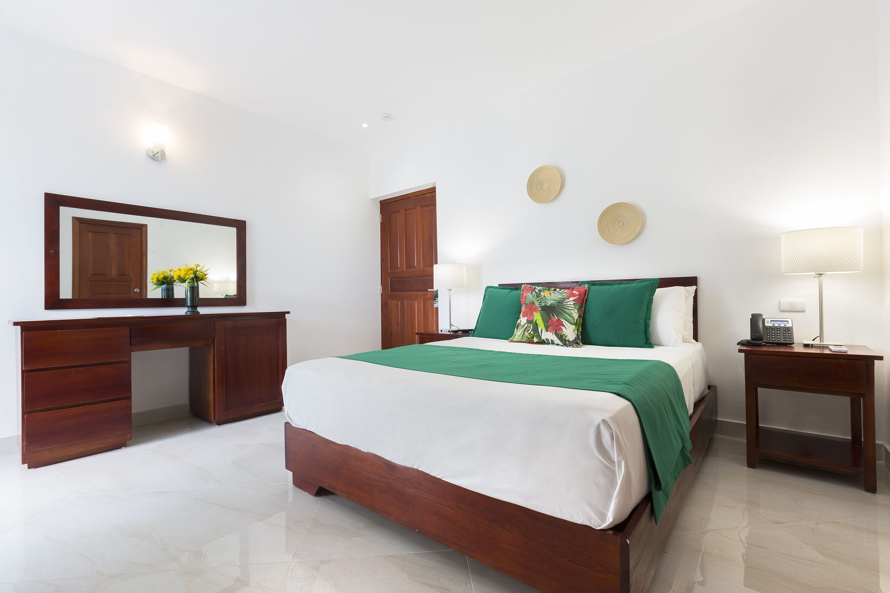 A bedroom with a bed, a wooden desk, a mirror, and a nightstand.