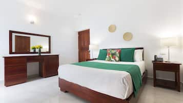 A bedroom with a bed, a wooden desk, a mirror, and a nightstand.