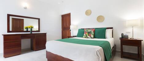 A bedroom with a bed, a wooden desk, a mirror, and a nightstand.
