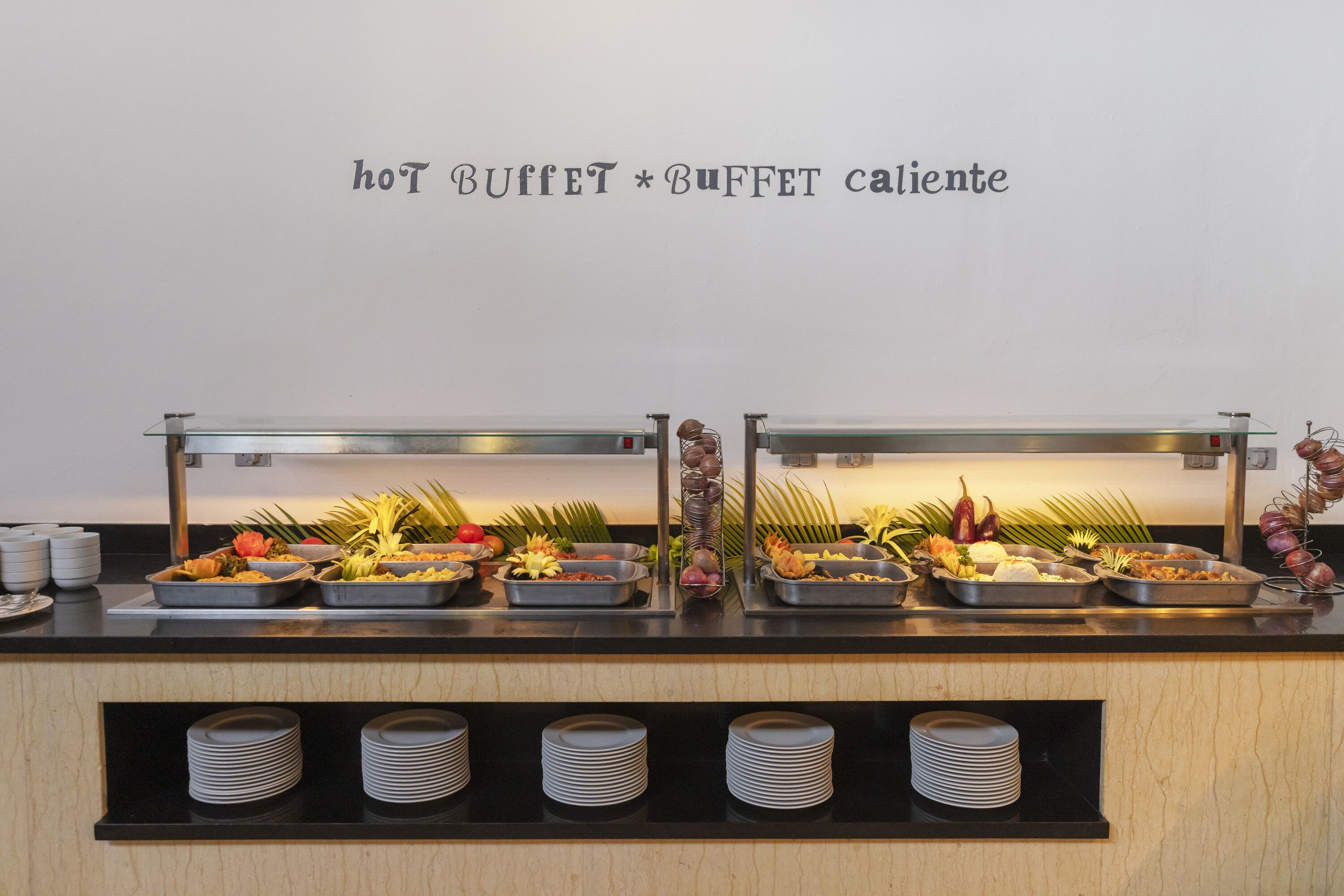 A buffet setup with multiple food trays and a sign above stating "hot buffet * buffet caliente".
