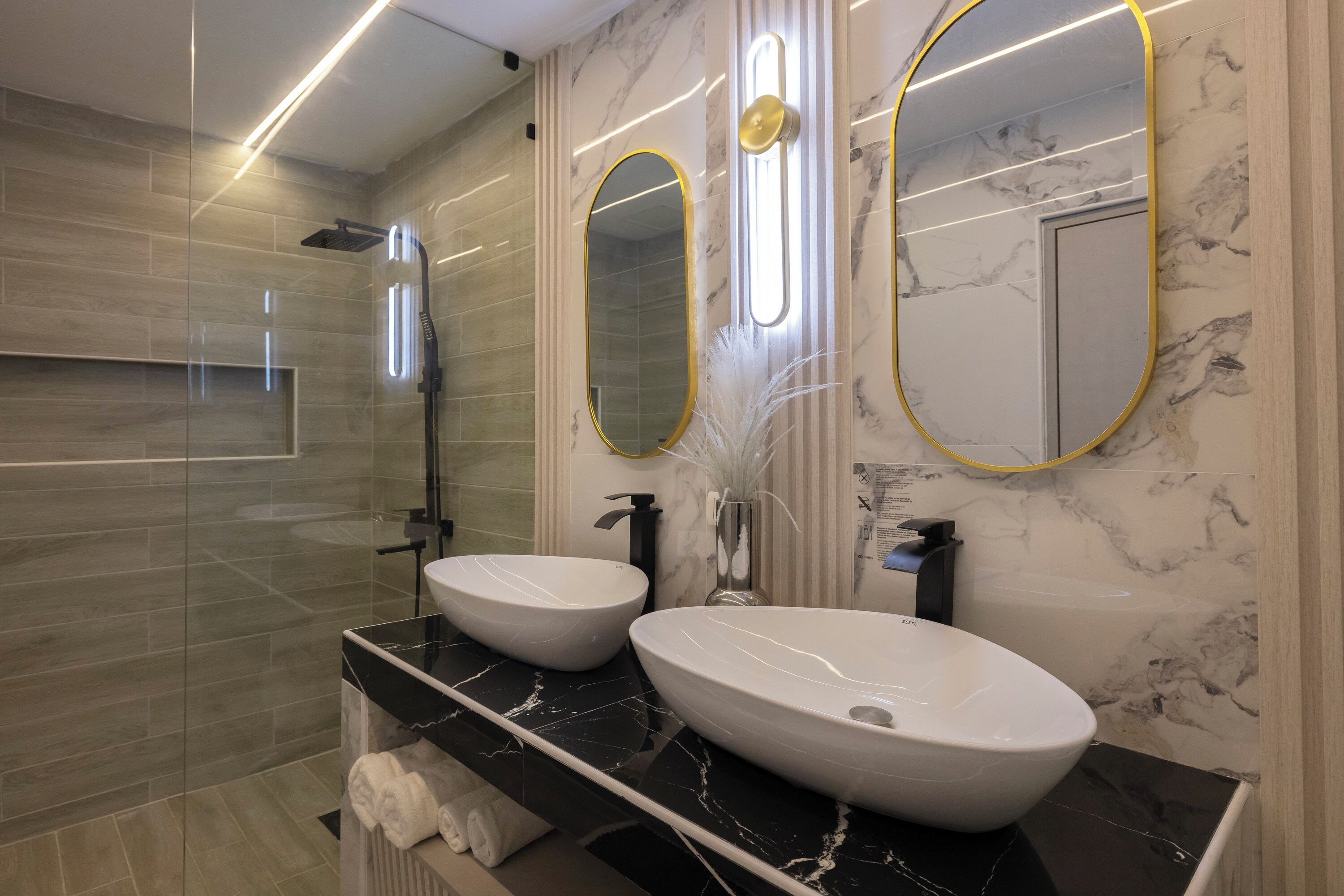 A modern bathroom with two sinks, a glass-enclosed shower, and marble walls.