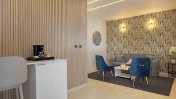Een moderne woonkamer met een bank, twee blauwe fauteuils, een koffieapparaat en een decoratieve wand.