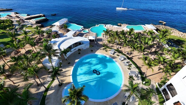 An aerial view of a resort with multiple swimming pools, palm trees, and a view of the ocean. - HM Alma de Bayahibe - Adults Only - All Inclusive (San Rafael del Yuma)