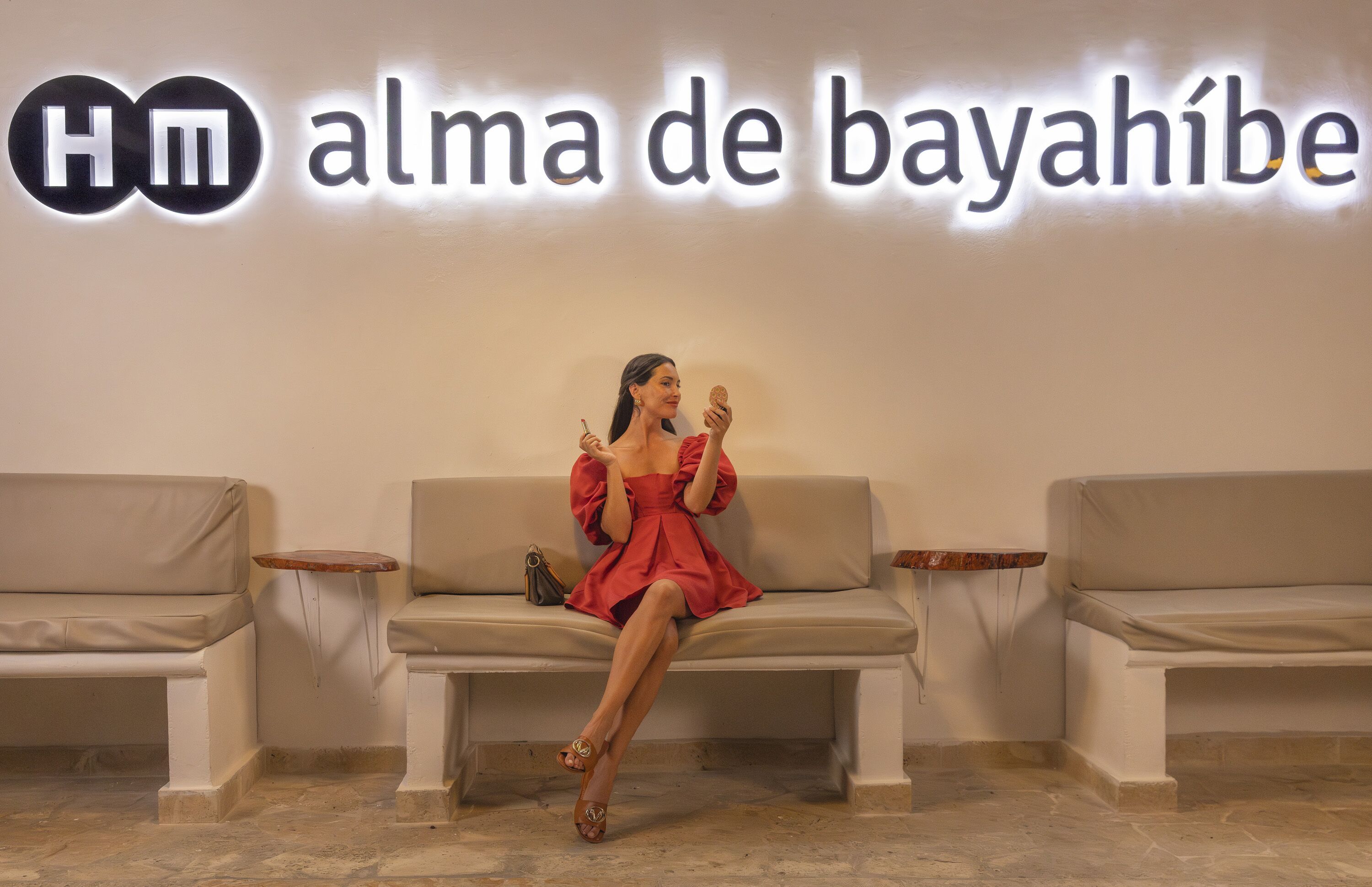 En kvinna sitter på en beige soffa framför en vägg med skylten ”Alma de Bayahibe”.