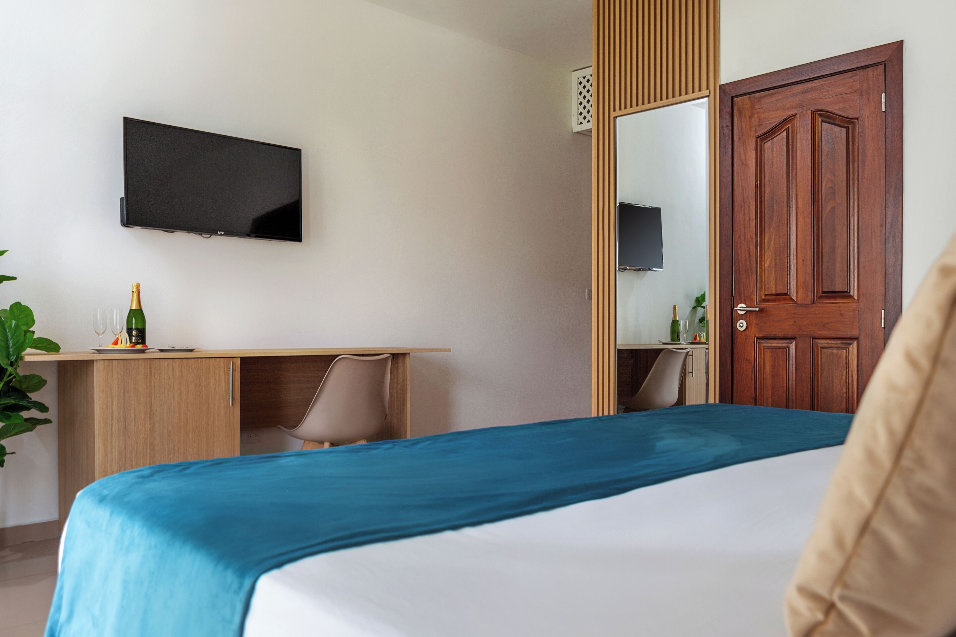 Habitación de hotel con cama, escritorio con silla, televisor montado en la pared y puerta de madera.