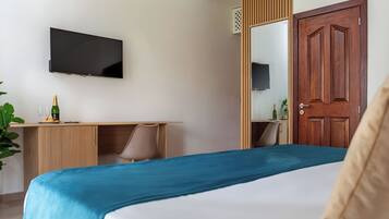 Habitación de hotel con cama, escritorio con silla, televisor montado en la pared y puerta de madera.
