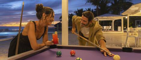A pool table with balls, a drink, and a person leaning over the table.