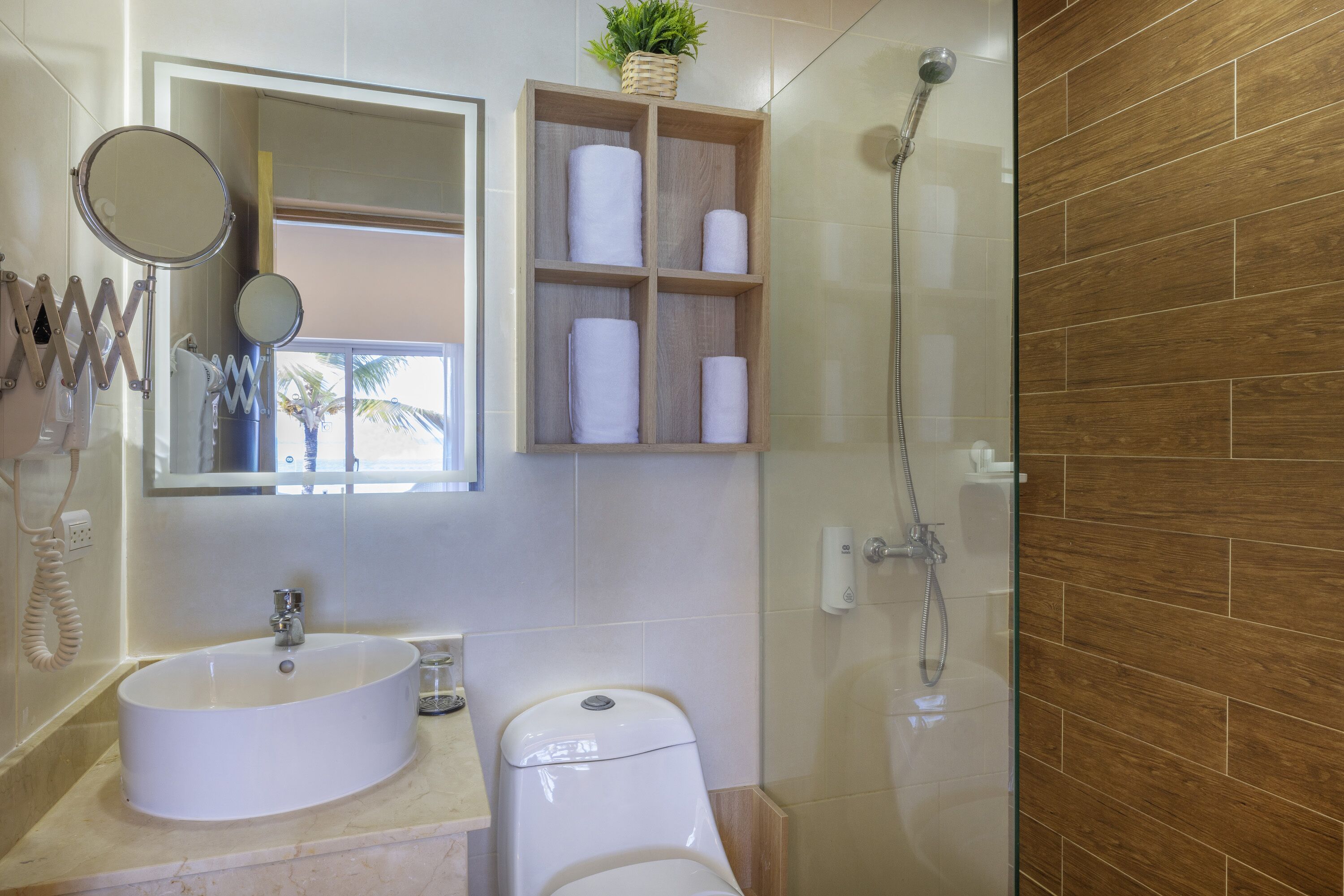 Un baño con lavabo, inodoro, espejo y estante de madera con toallas.