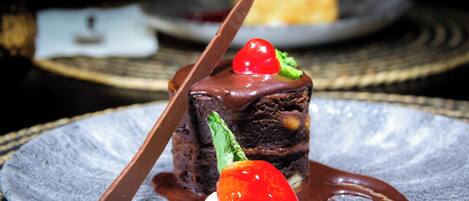 A dessert on a plate with a chocolate topping, a strawberry, and a mint leaf.