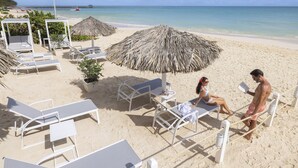 A beachside lounge area with sun loungers, a thatched umbrella, and a view of the ocean. - HM Bavaro Beach – Adults Only (Punta Cana)