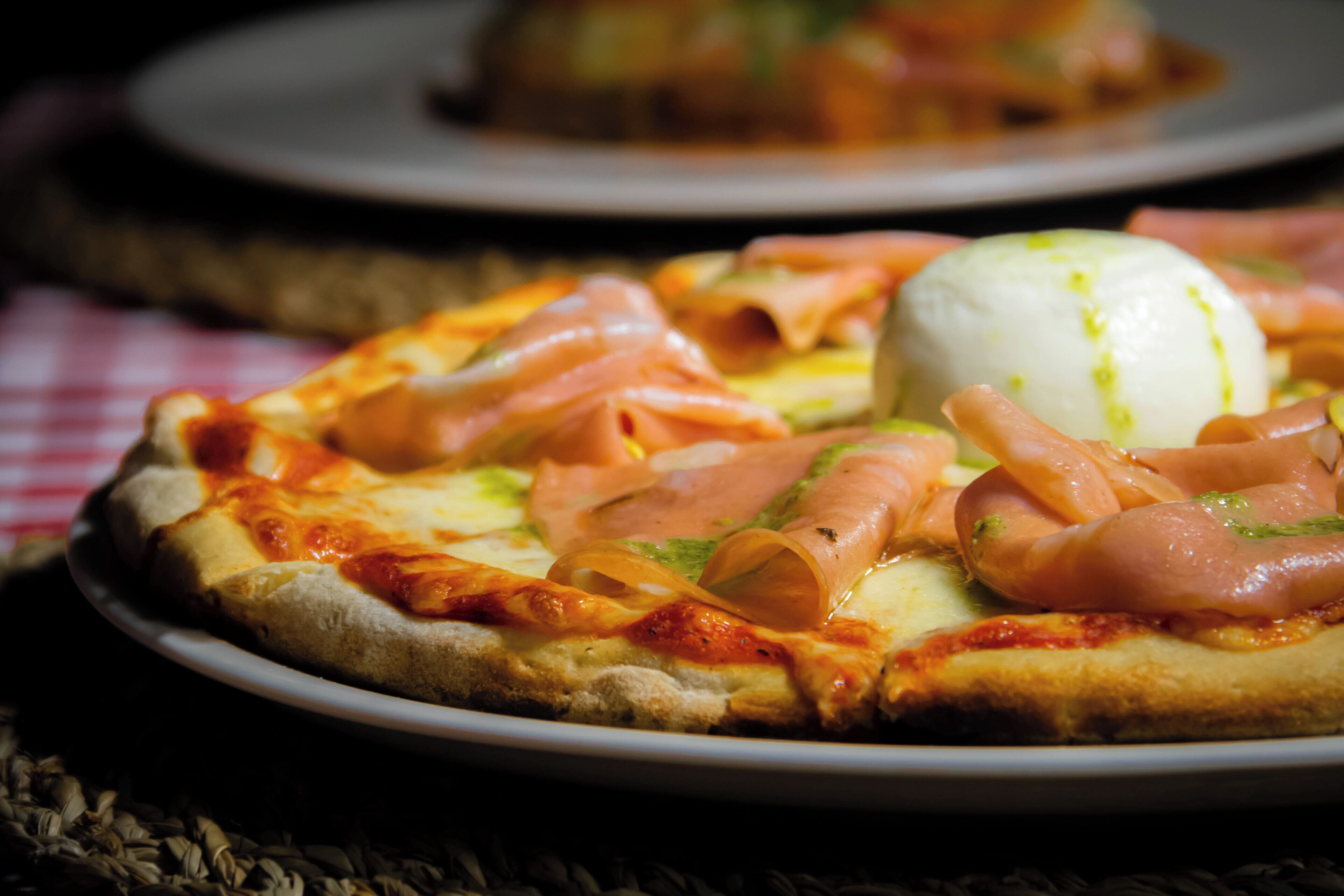 A pizza with ham and a ball of mozzarella on a plate.