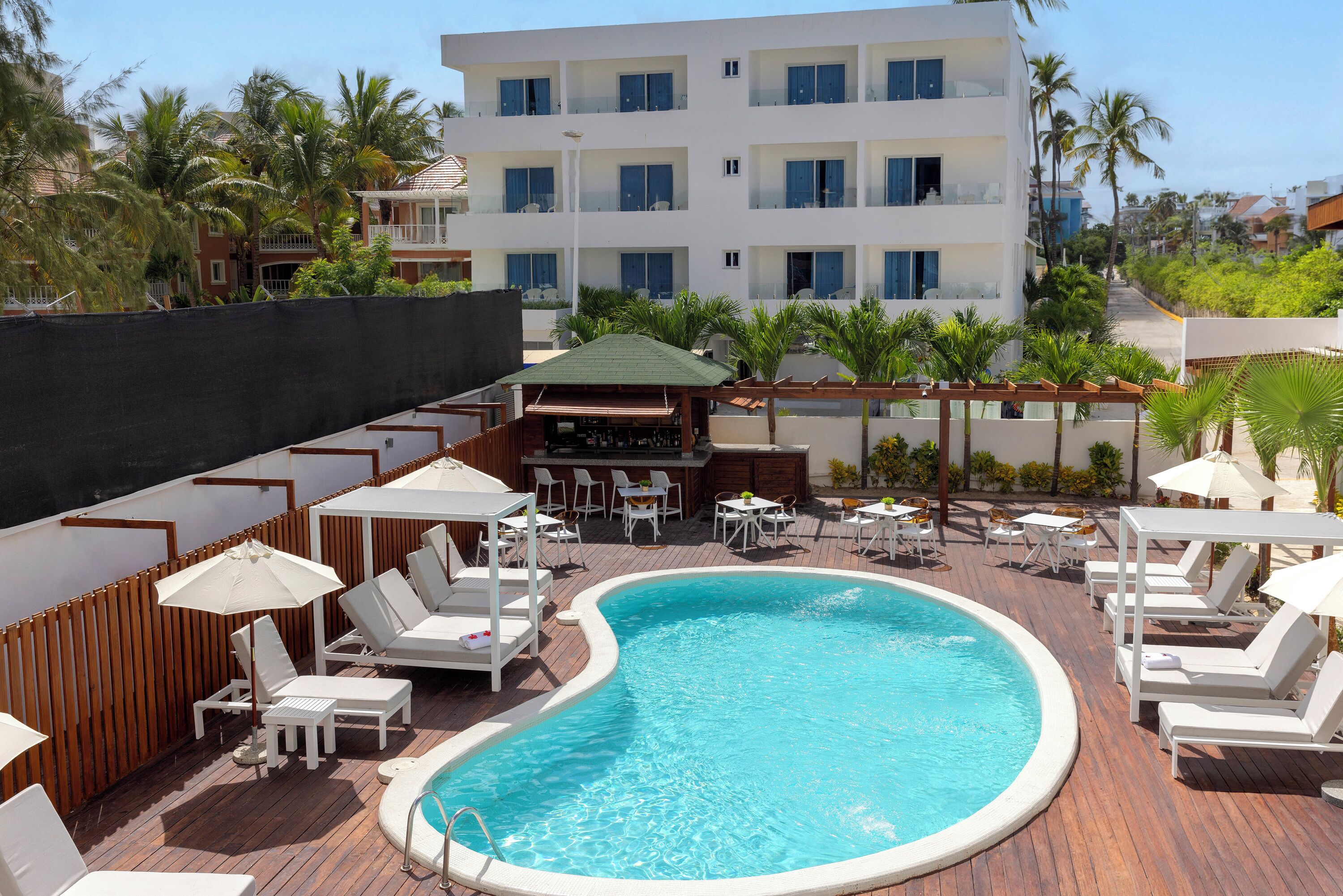 Un espace piscine avec des chaises longues et des parasols, un bar et un bâtiment avec des balcons en arrière-plan.