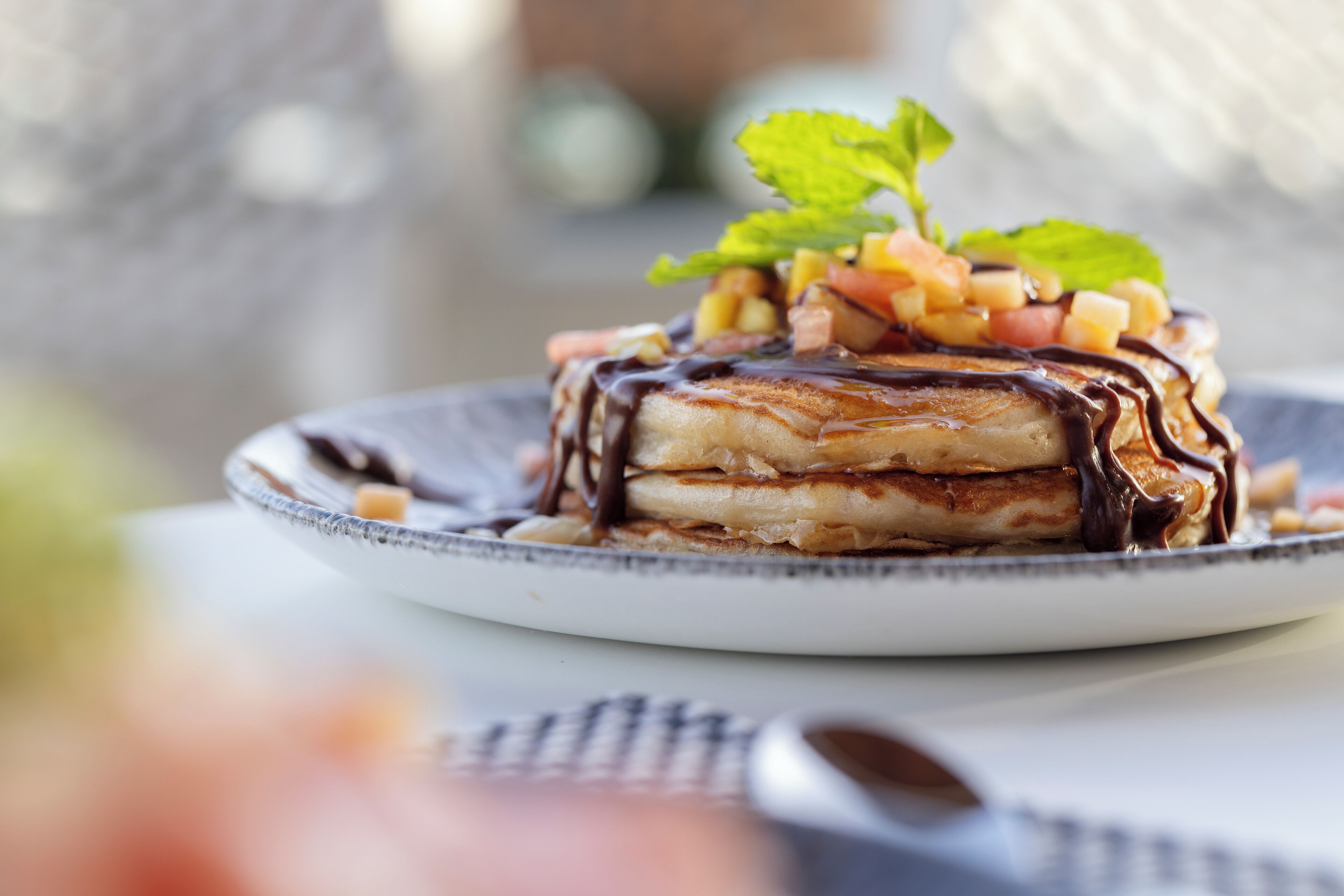 Una pila de panqueques con salsa de chocolate y fruta sobre un plato.
