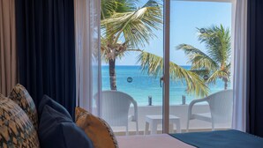 A hotel room with a bed, a view of the ocean, and a balcony with white chairs and a table. - HM Bavaro Beach – Adults Only (Punta Cana)