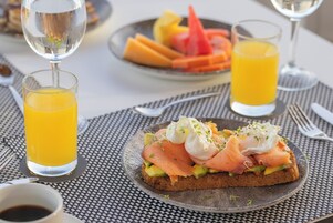 Un desayuno con una tostada de salmón ahumado y aguacate, un vaso de zumo de naranja y un bol de fruta.