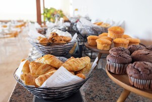 Una mesa de bufé con diversas opciones de repostería, incluyendo croissants, muffins y pasteles.