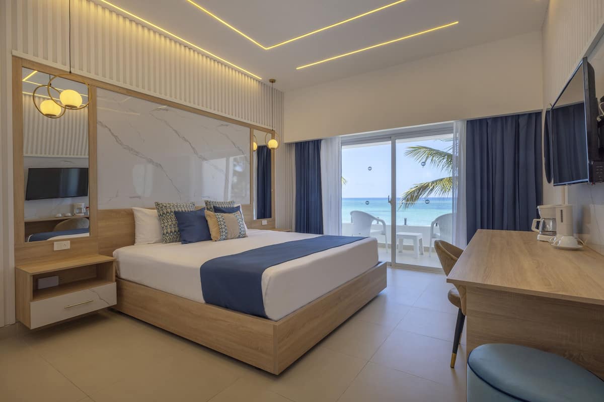Habitación de hotel moderna con una cama grande, un escritorio, un televisor y un balcón con vistas al mar.