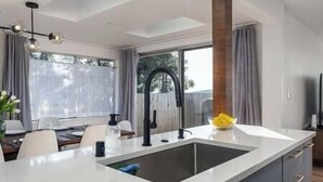 A modern kitchen with a large island, a built-in sink, and a dining area with a table and chairs. - 5BR/4BA: Spacious Step-Free Main Level, Relaxing Views, Next to Chamber Bay Golf (University Place)