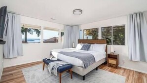 A bedroom with a large bed, a bedside table, a bench, and a view of the sea through the windows. - 5BR/4BA: Spacious Step-Free Main Level, Relaxing Views, Next to Chamber Bay Golf (University Place)