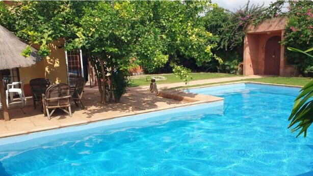 Ein Swimmingpool mit klarer, blauer Wasseroberfläche, umgeben von einer Terrasse mit Stühlen und einem kleinen Tisch.