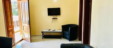 A hallway with a TV mounted on the wall, a small table with chairs, and a door leading outside.