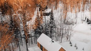 Eine moderne, zweistöckige Holzhütte, umgeben von einem verschneiten Wald.