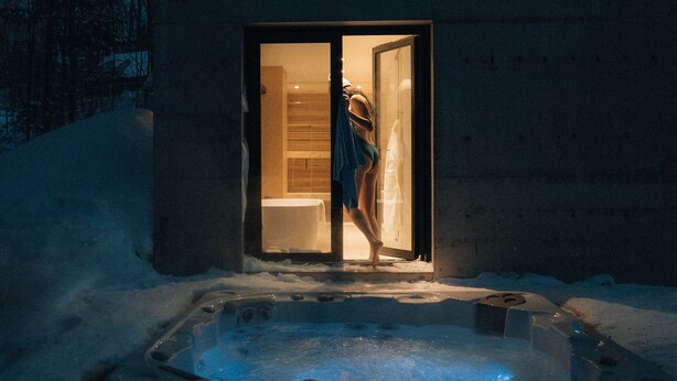 Ein modernes Gebäude mit Glastür und einem Whirlpool im Vordergrund, Schnee auf dem Dach.